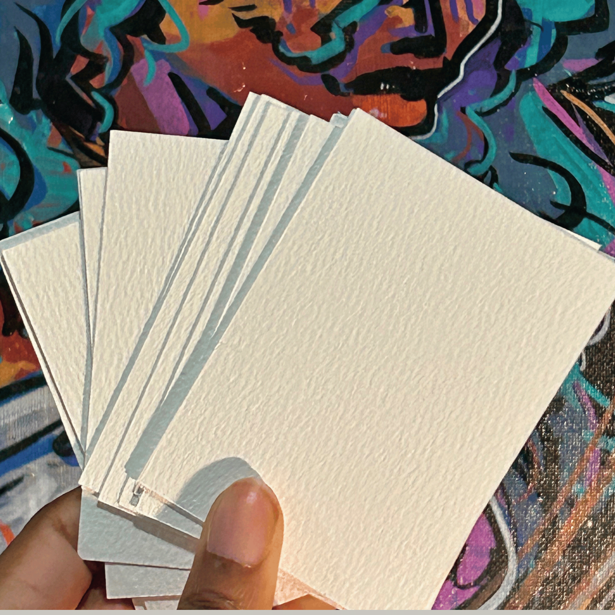 Hand holding a stack of white playing cards against a colorful abstract background